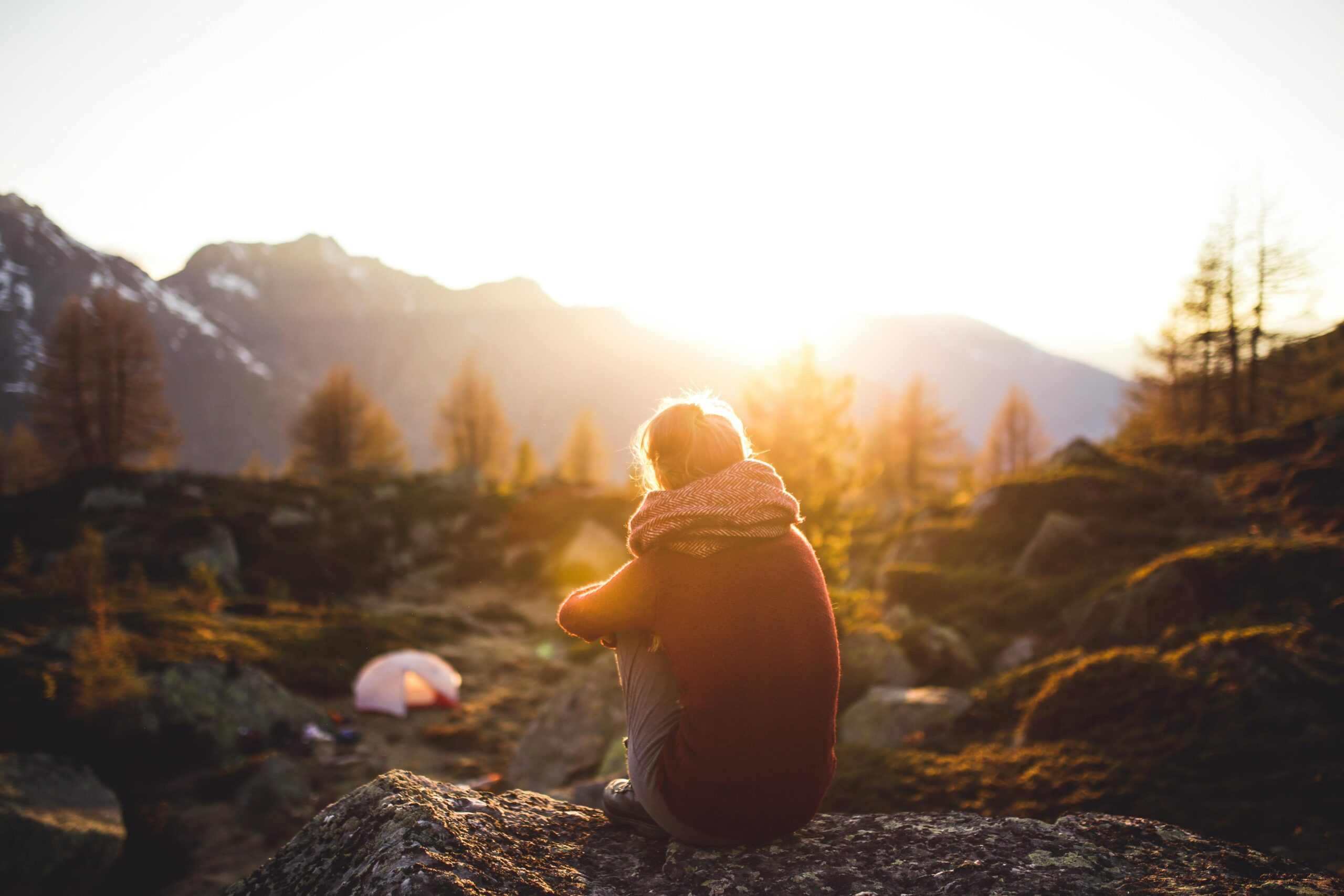 A person sitting on a rock at golden hour, looking thoughtfully into the distance.