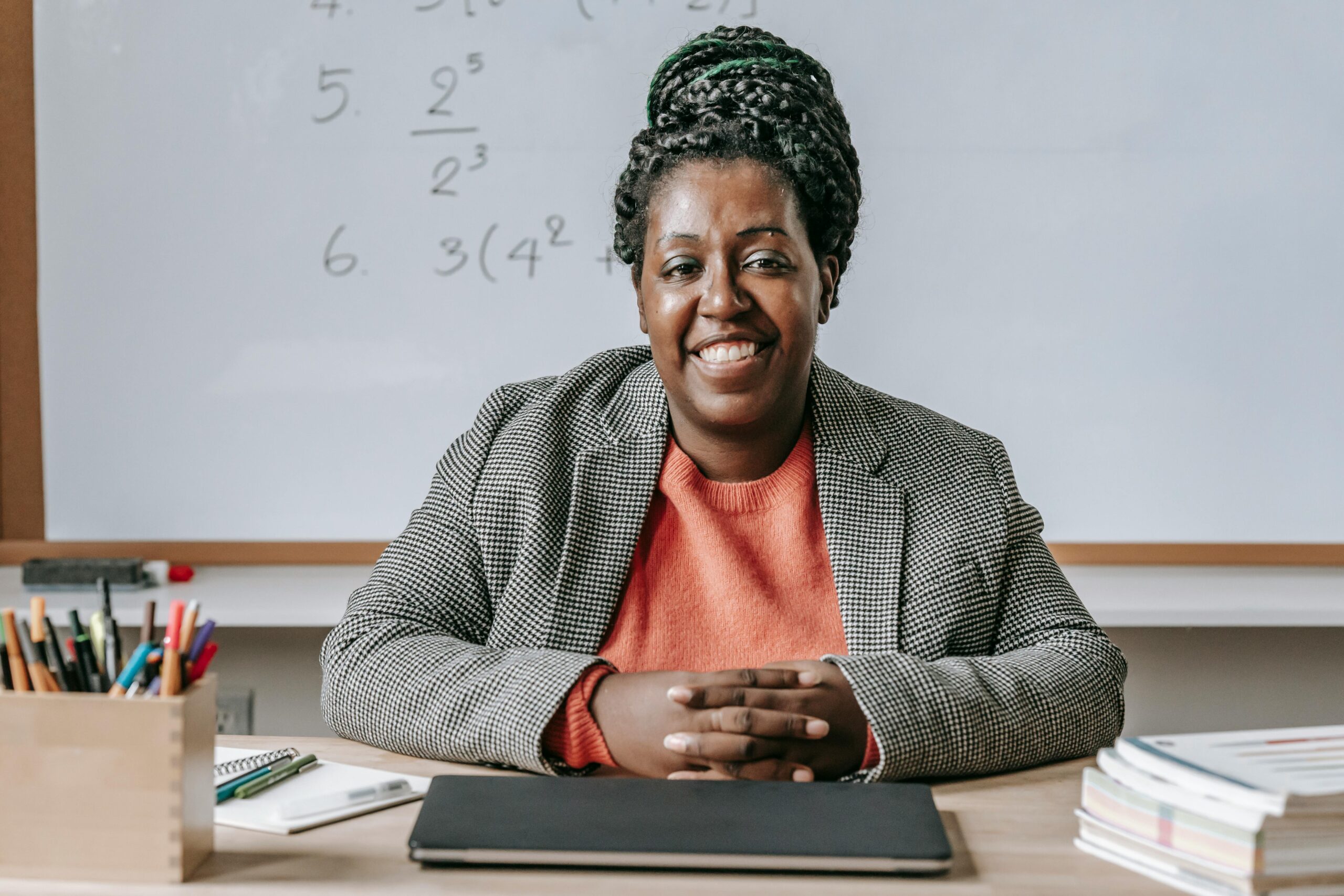 A cheerful Black woman sitting at a table, smiling brightly with her arms crossed, radiating positivity and confidence.