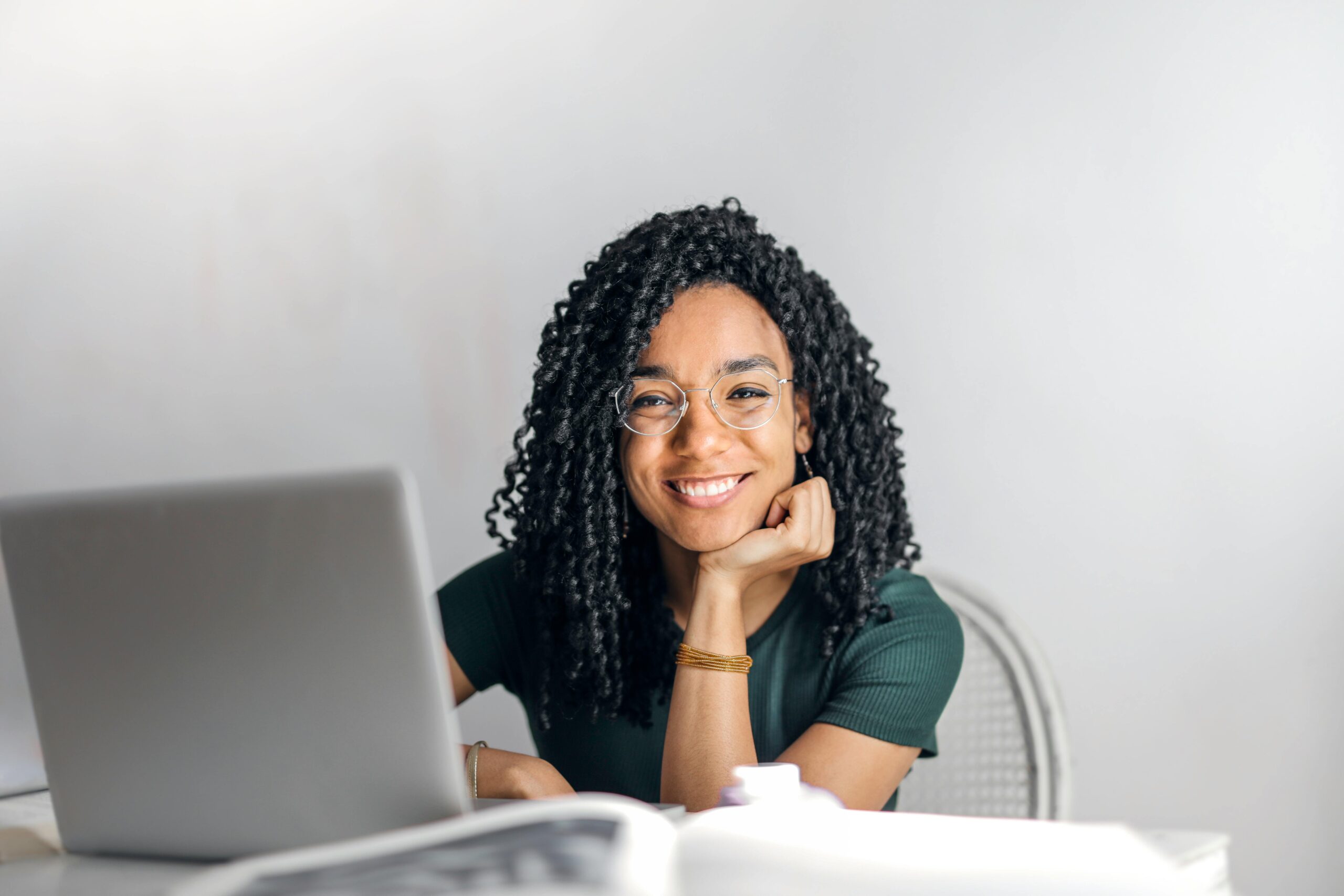 A smiling woman sitting at a table with a laptop, enjoying a productive morning routine and creating a positive start to her day.